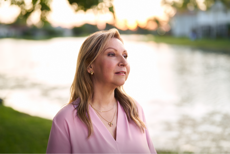 Mujer al aire libre junto al agua con expresión reflexiva.